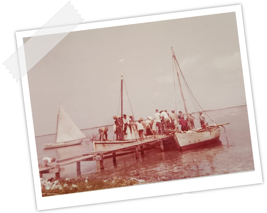 A group of people gather on a wooden dock beside two boats on calm water.